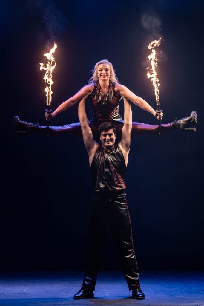 Two fire performers with flaming swords in an acrobatic post